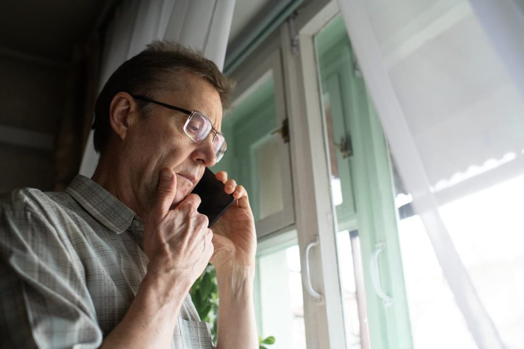 Beyond the Stamp: The Vital Role of a Notary Public in Fraud Prevention 8 Concerned man on phone near window, symbolizing the importance of notary publics in fraud prevention and verifying identity at NotaryPublic24