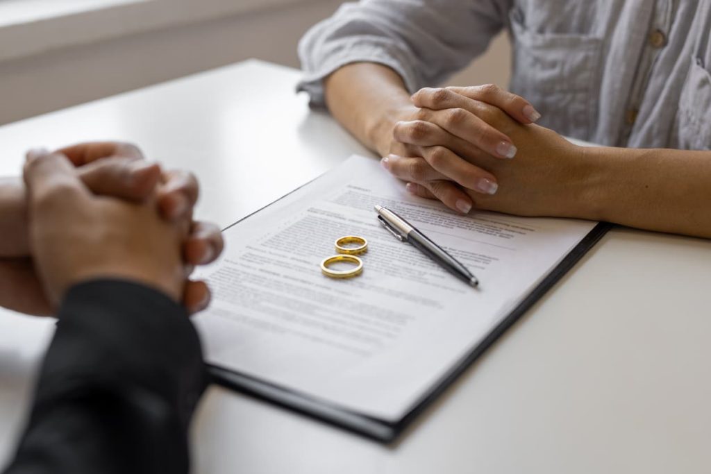 Understanding the Decree Nisi and Decree Absolute: A Comprehensive Guide 1 Close-up of two people sitting across a table with a divorce agreement, wedding rings, and a pen in focus — symbolizing the legal separation process involving Decree Nisi and Decree Absolute, relevant for international document legalization and notary services at NotaryPublic24.com
